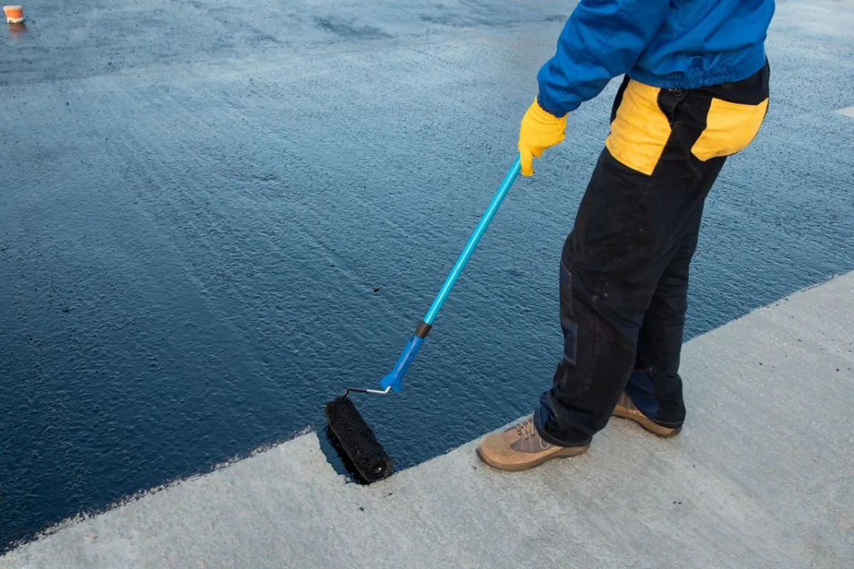 a worker applies bitumen mastic to concrete